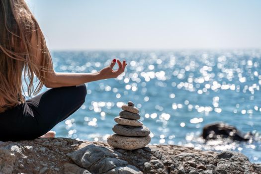Young woman in black leggings and black top with long flowing hair practicing stretching outdoors by the sea on a sunny day. Women's yoga, fitness, pilates. The concept of a healthy lifestyle, harmony.
