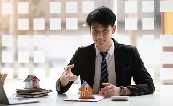 Miniature house in the hands of an Asian bussinessman real estate agent home loan working at the office. Looking at the camera.