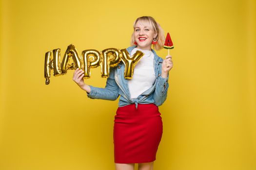 Cheerful girl with inflatable letters HAPPY.Stock photo portrait of attractive girl with red lips holding shining bright inflatable word HAPPY. Isolate on orange background.