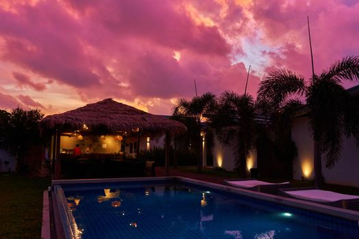 A gentle sunset sky over a thatched bungalow. An exotic resort in the tropics