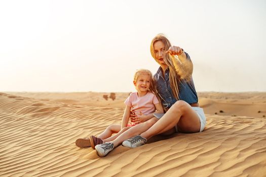 Mother and daughter sitting together on sand dune in the Dubai desert