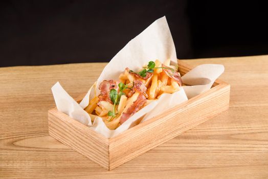 French fries with fried bacon on parchment in wooden box on the table