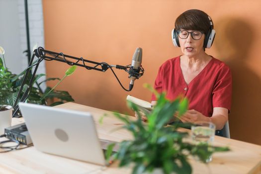 Portrait of mature woman wearing headphones and talking at online radio station - podcast and broadcast concept