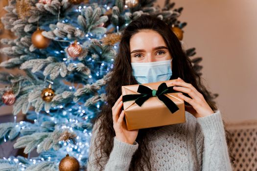 Girl in a medical mask with a Christmas present. celebration of the new year on self-isolation. Pandemic coronavirus covid-19 concept.
