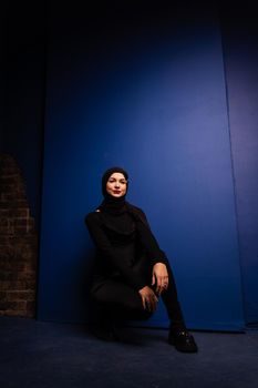 Fashion muslim model in black hijab is posing on blue background in studio. Islam religion.