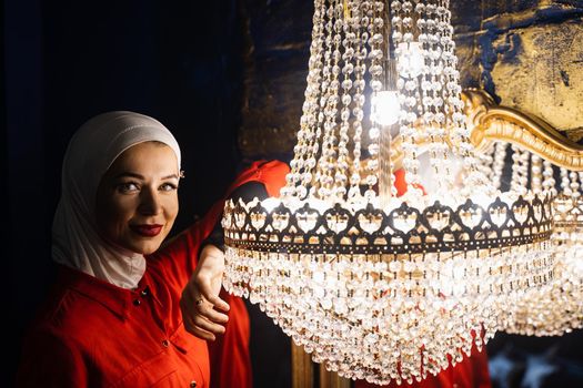 Fashion muslim model near big expensive chandelier. Islamic religion. Girl near mirrors.