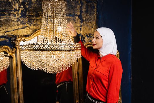 Fashion muslim model near big expensive chandelier. Islamic religion. Girl near mirrors.