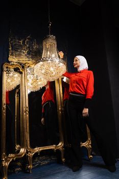 Fashion muslim model is posing near big expensive chandelier. Islamic religion. Girl near mirrors.