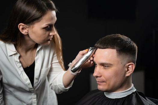 Trimming bangs of handsome man in barbershop. Woman hairdresser making hair style.