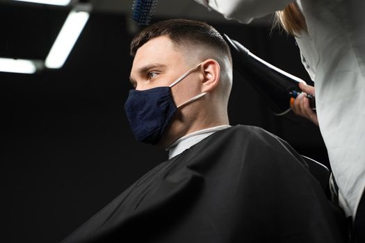 Barbershop service at coronavirus covid-19 period. Drying hair after cutting in barbershop for handsome man. Using mask.