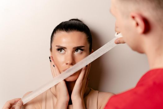 Model with glued mouth. Man covers woman mouth with tape. Stop talking.