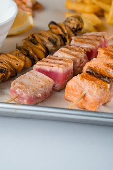 Barbecue seafood kebab with grilled mussels, tuna, salmon on a wooden skewer with white sauce and lemon.