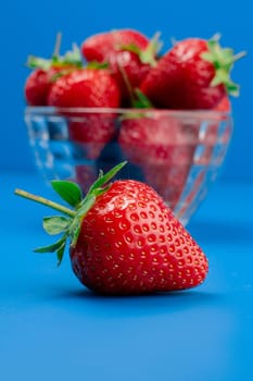 Bunch of strawberry in bowl on blue background. Yummy summer fruit.