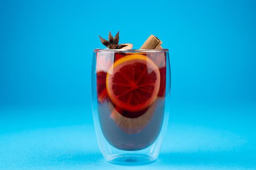 Mulled wine on blue background. Alcohol punch in double glass cup. Drink with orange, anise star, cinnamon and apple.