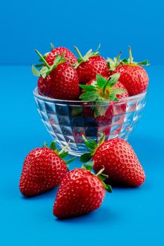 Bunch of strawberry in bowl on blue background. Yummy summer fruit.