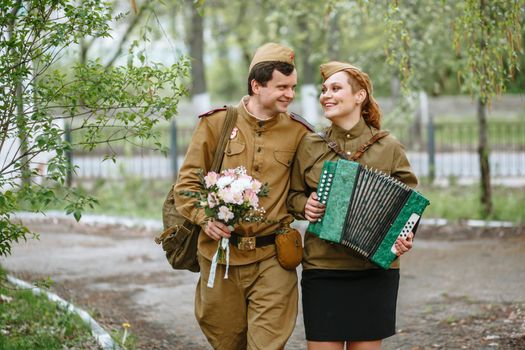 People in Soviet military uniforms. A soldier walks down the alley, hugging a military girl playing an accordion