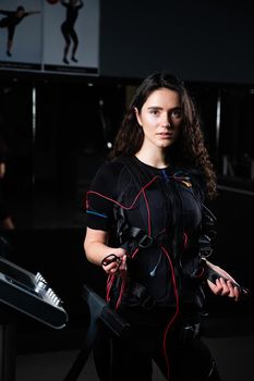 Girl in EMS suit in gym. Sport training in electrical muscle stimulation suit. Making physical exercises