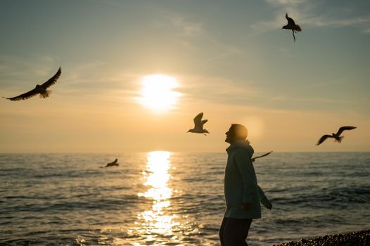 Caucasian woman feeding seagulls at sunset by the sea.