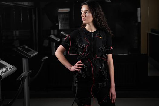 Girl in EMS suit in gym. Sport training in electrical muscle stimulation suit.