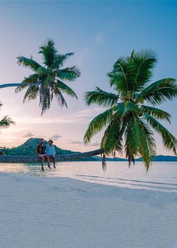 Praslin Seychelles tropical island with withe beaches and palm trees, couple men and woman with palmtree watching sunset
