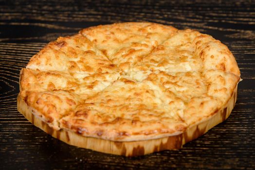 Tortilla baked with cheese on a wooden plate on a dark wooden table. Cheese pastries with a crispy crust