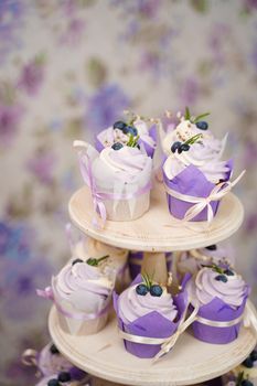 Cupcakes with cream in a paper tulip form, decorated with blueberries, rosemary, flowers, tied with a ribbon. Vanilla cupcakes with lavender cream. Thematic muffins