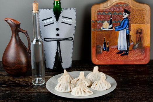 Khinkali on a gray plate against the background of bottles in a Georgian-style decoration, a jug, a board with a thematic pattern on a dark wooden table
