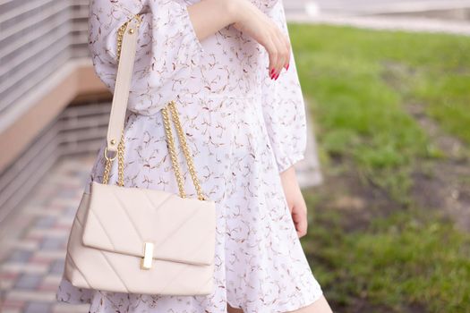 close up of woman in white dress holding fashionable beige purse outside. Product photography. stylish handbag for women