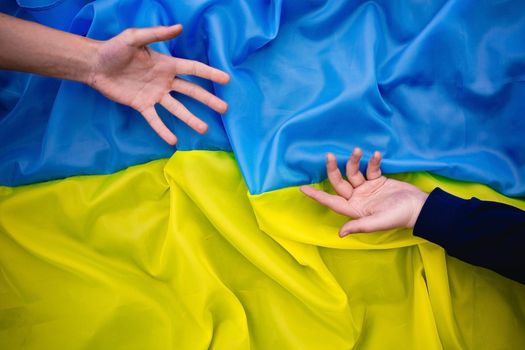 Hands reach out to each other against the background of the Ukrainian flag.