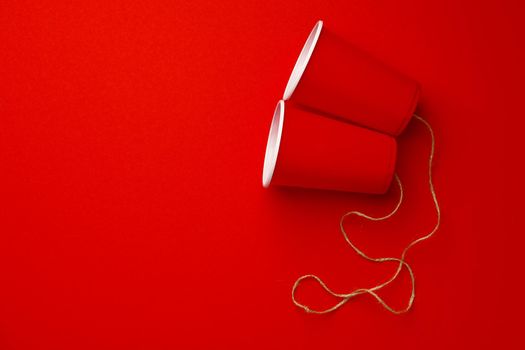 Red plastic cups connected with a thread on red background