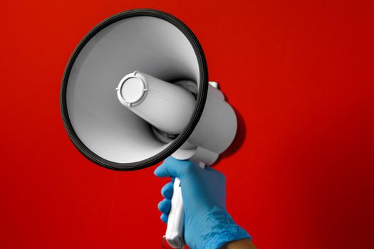 Human hand in medical glove holding electronic megaphone on red background