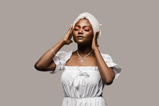 Beauty portrait of black muslim woman weared white dress and headscarf on gray background. Softness and wellness of body and skin.