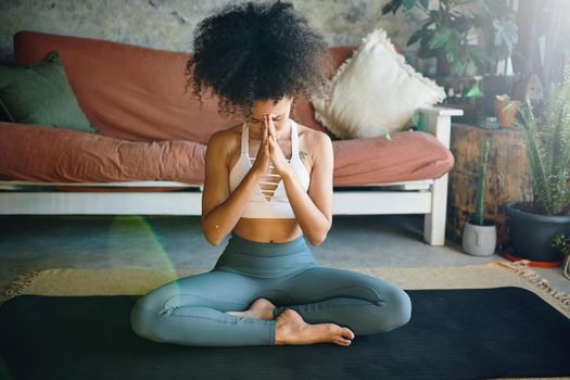 Shot of a young woman meditating in her living room - Stock Photo