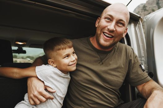Happy father and son sitting in car trunk on road trip