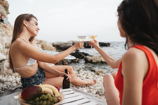 Two young female friends having picnic on a beach drinking cocktails