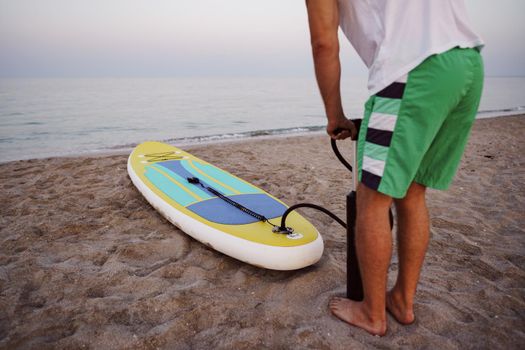 Close up of man prepares to paddle surf on a beach inflating sup board