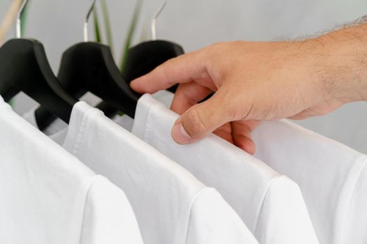Male hand holds hanger with blank white t-shirt