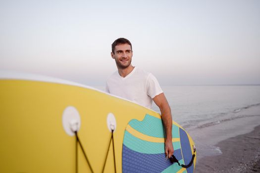 Young man carrying sup board after water surf session