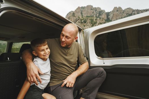 Happy father and son sitting in car trunk