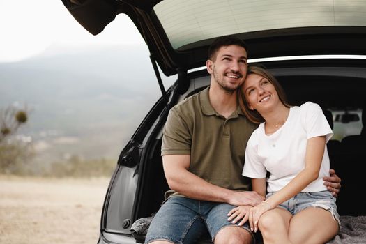 Young happy couple on a road trip sitting in car trunk
