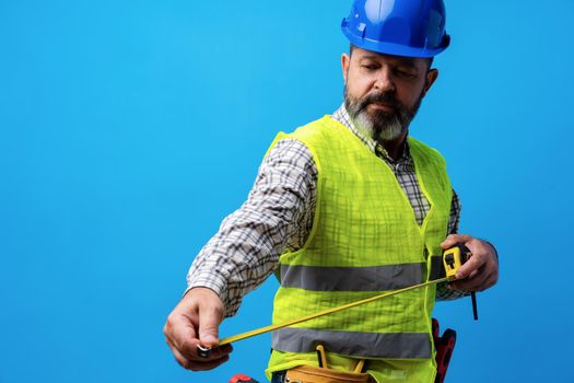 Male builder holding measuring roulette against blue background