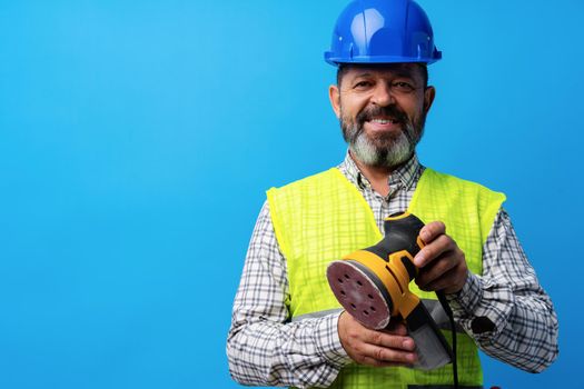 Industrial builder holding grinder machine against blue background