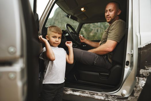 Father and little son standing near car on road trip