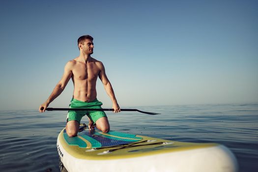 Young fit man on paddle board floating on lake.