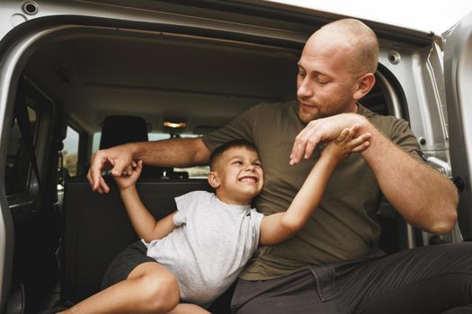 Happy father and son sitting in car trunk on road trip
