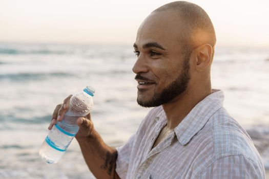 African american man drinking water from the bottle on beach