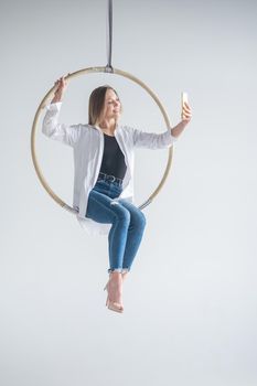 Caucasian woman gymnast on an aerial hoop takes a selfie on a smartphone.