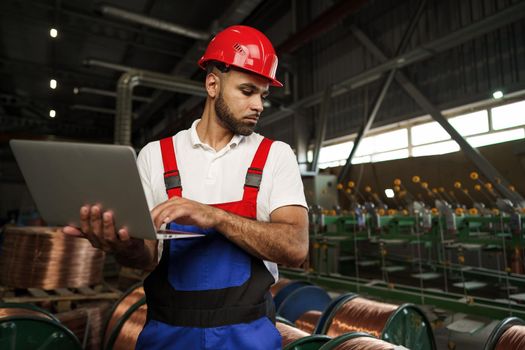 Industrial worker with laptop working in a cable production plant