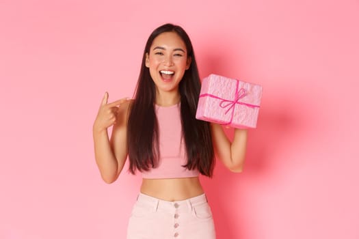 Holidays, celebration and lifestyle concept. Beautiful happy asian girl pointing at herself, its her birthday, receive gift wrapped in pink paper, smiling broadly over studio background.