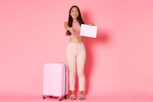 Travelling, holidays and vacation concept. Full-length of friendly smiling asian girl tourist standing near suitcase with paper sign and extend hand for handshake, meeting in airport